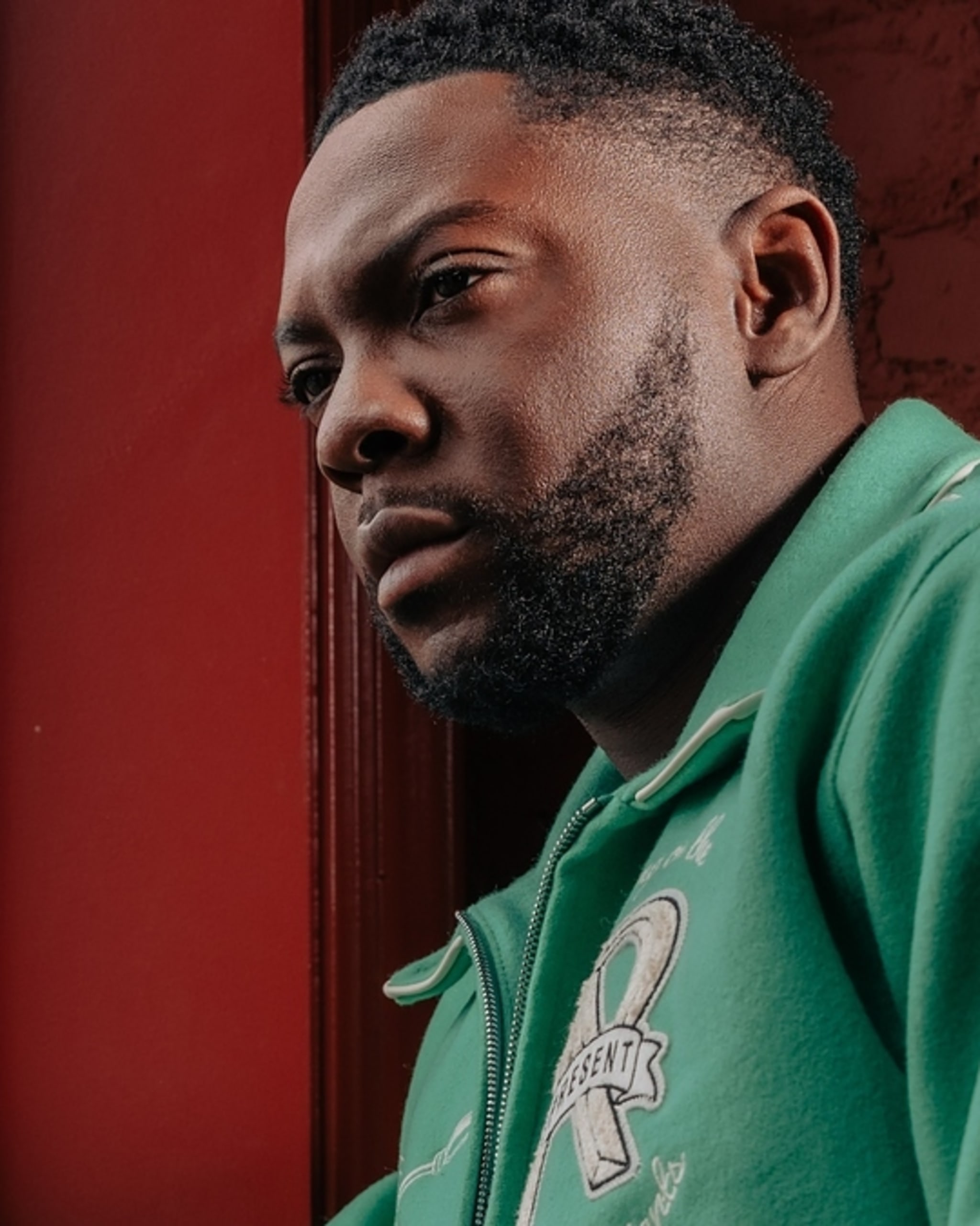 Actor dressed in a casual jacket looks out a window with a contemplative expression