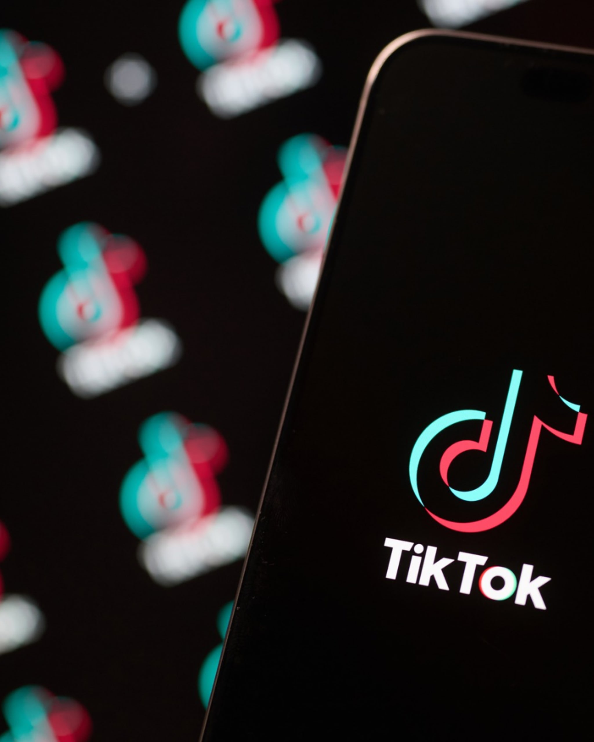 A smartphone displaying the TikTok logo on its screen, with multiple blurred TikTok logos in the background.