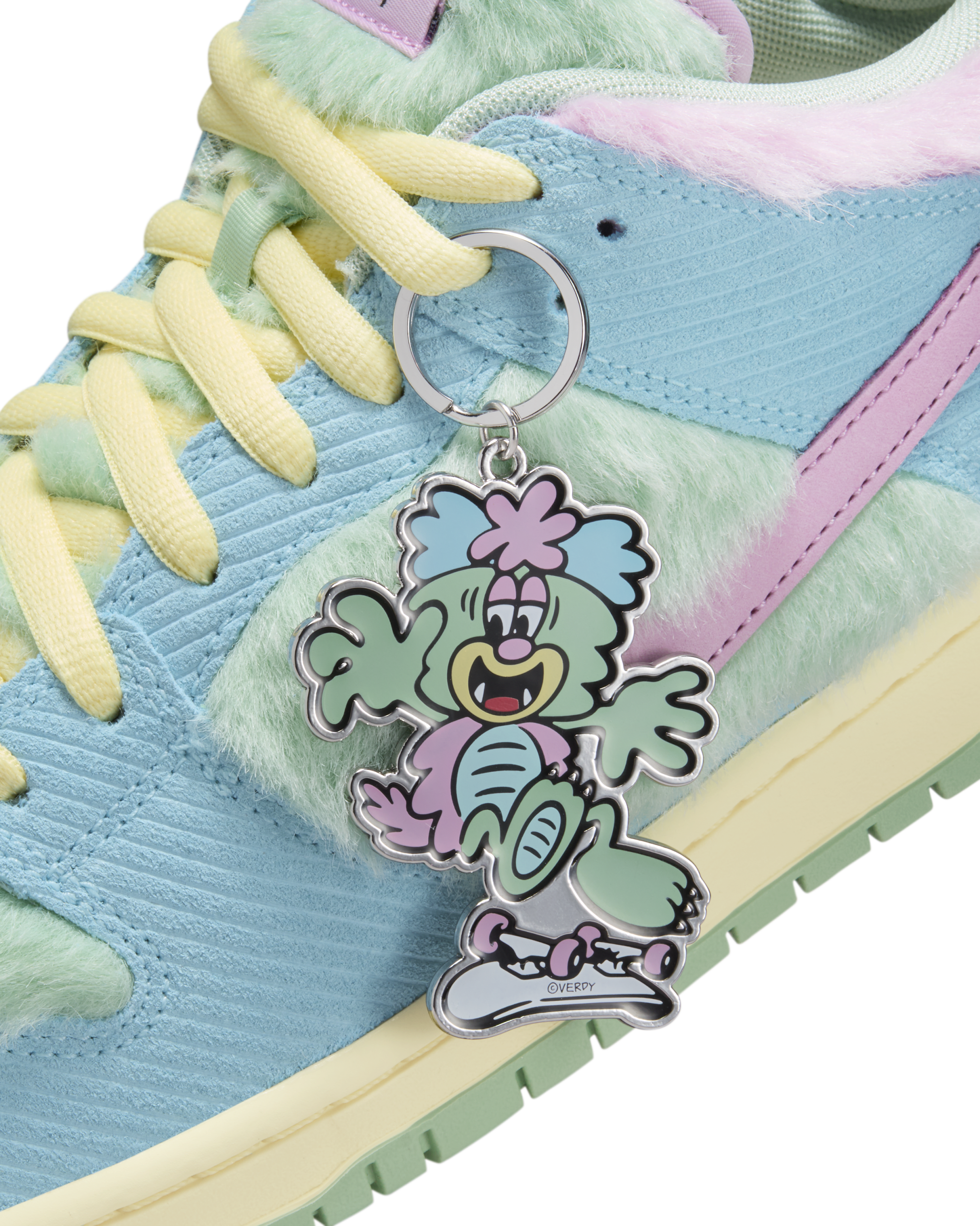 A close-up of a colorful sneaker with pastel blue, green, and pink fur accents, featuring a cartoon character keychain attached to the laces.